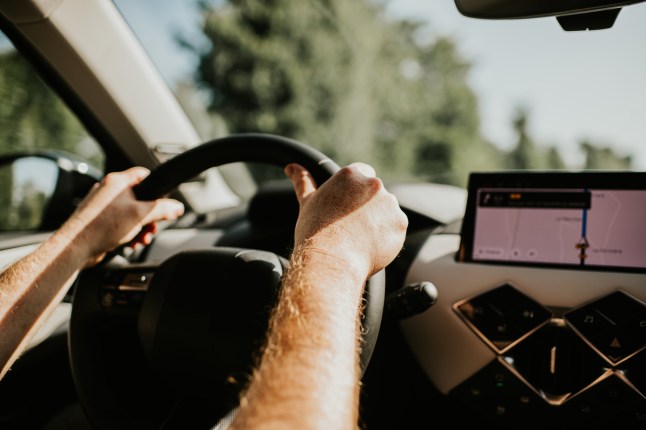 A man drives a modern vehicle, utilising a sat nav displayed on a dashboard screen