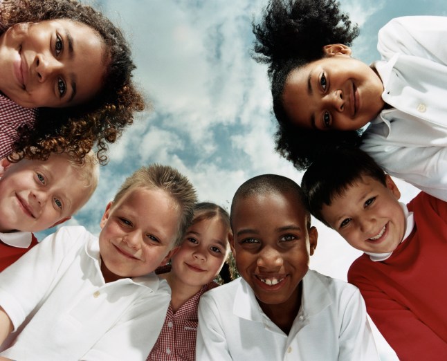 View Directly Below of Seven Primary School Children Huddled Together Looking at the Camera