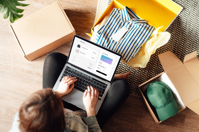Young woman doing online shopping with laptop sitting on the floor at home