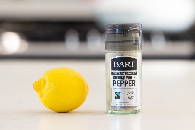 A jar of white pepper and a lemon on a kitchen counter